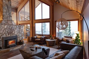 A cozy living room with a stone fireplace, large windows, and comfortable seating. - Big White Is Calling -  Big White BC (Beaverdell)