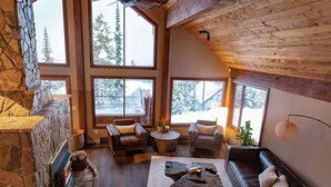 A cozy living room with a stone fireplace, large windows, and a wooden ceiling. - Big White Is Calling -  Big White BC (Beaverdell)