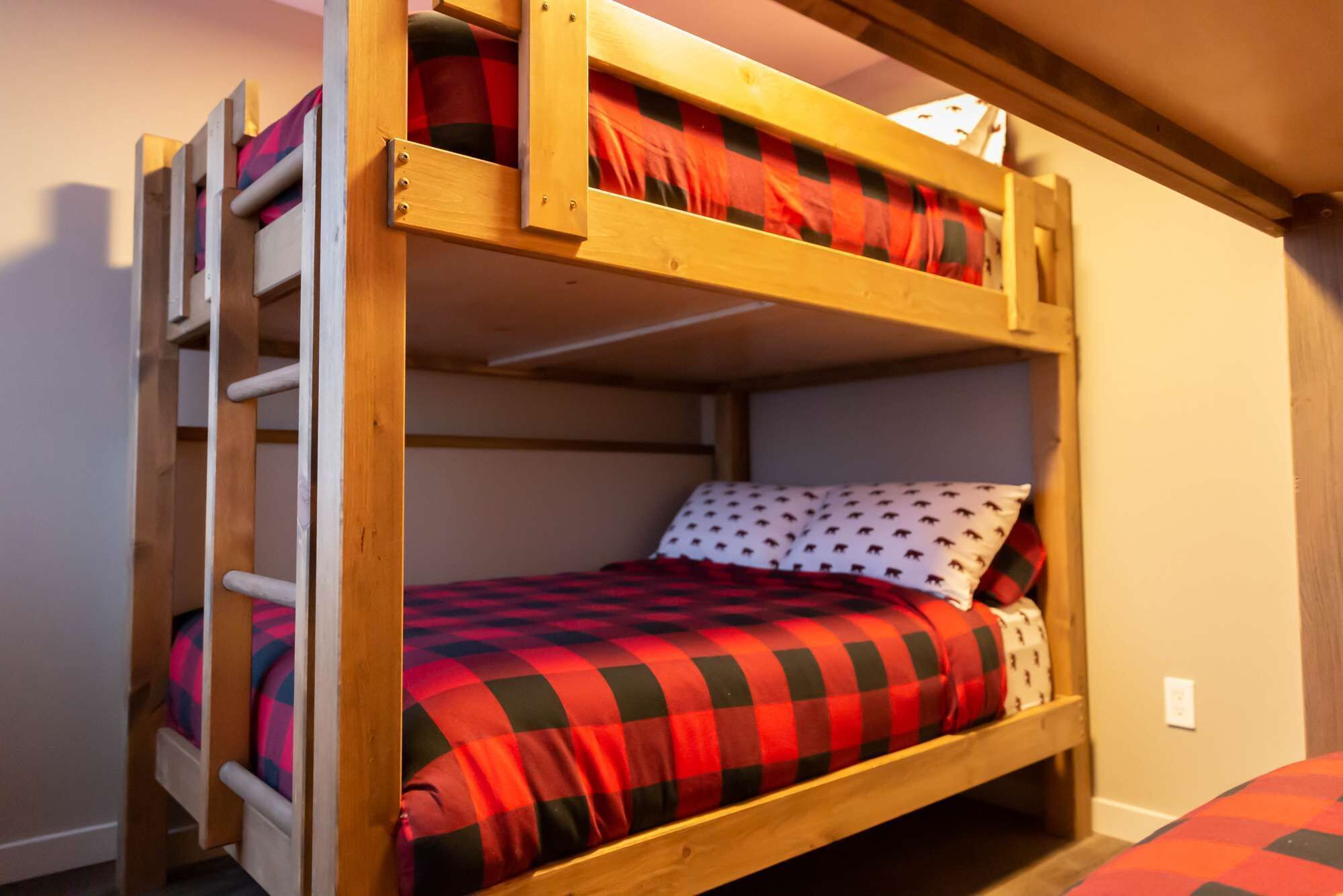 A bunk bed with a ladder, a red and black checkered bedspread, and a pillow with a pattern.