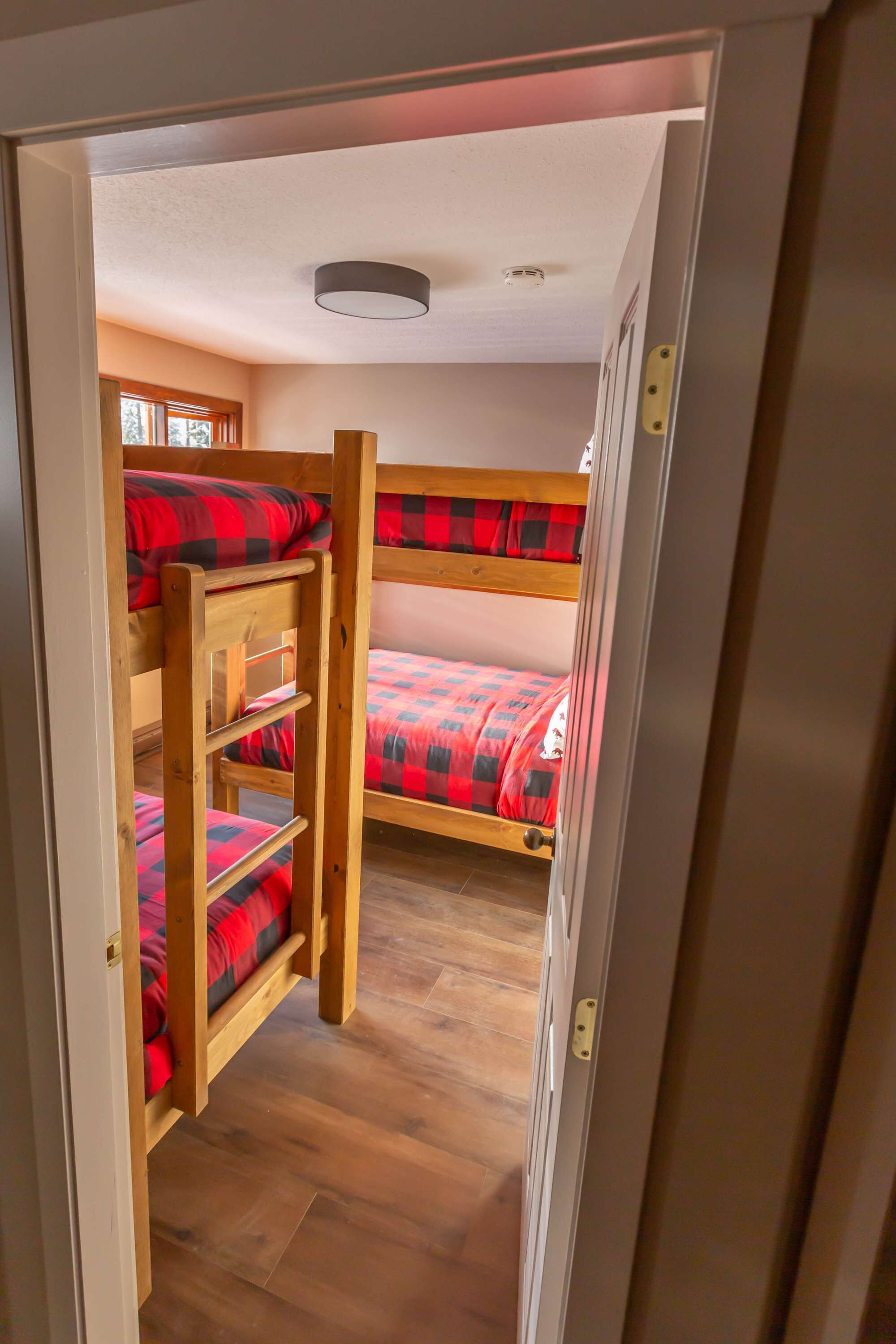 Een kamer met stapelbedden, houten vloeren en een deur naar een andere kamer.