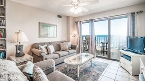 A living room with a sofa, coffee table, and TV, a balcony with a view, and a ceiling fan. - 3 Bedroom/2 Bath Oceanfront Timeshare in Myrtle Beach (Murrells Inlet)