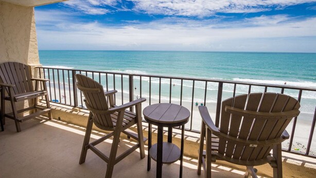 A balcony with four wooden Adirondack chairs and a small round table, overlooking a beach with the ocean and a clear sky. - 3 Bedroom/2 Bath Oceanfront Timeshare in Myrtle Beach (Murrells Inlet)