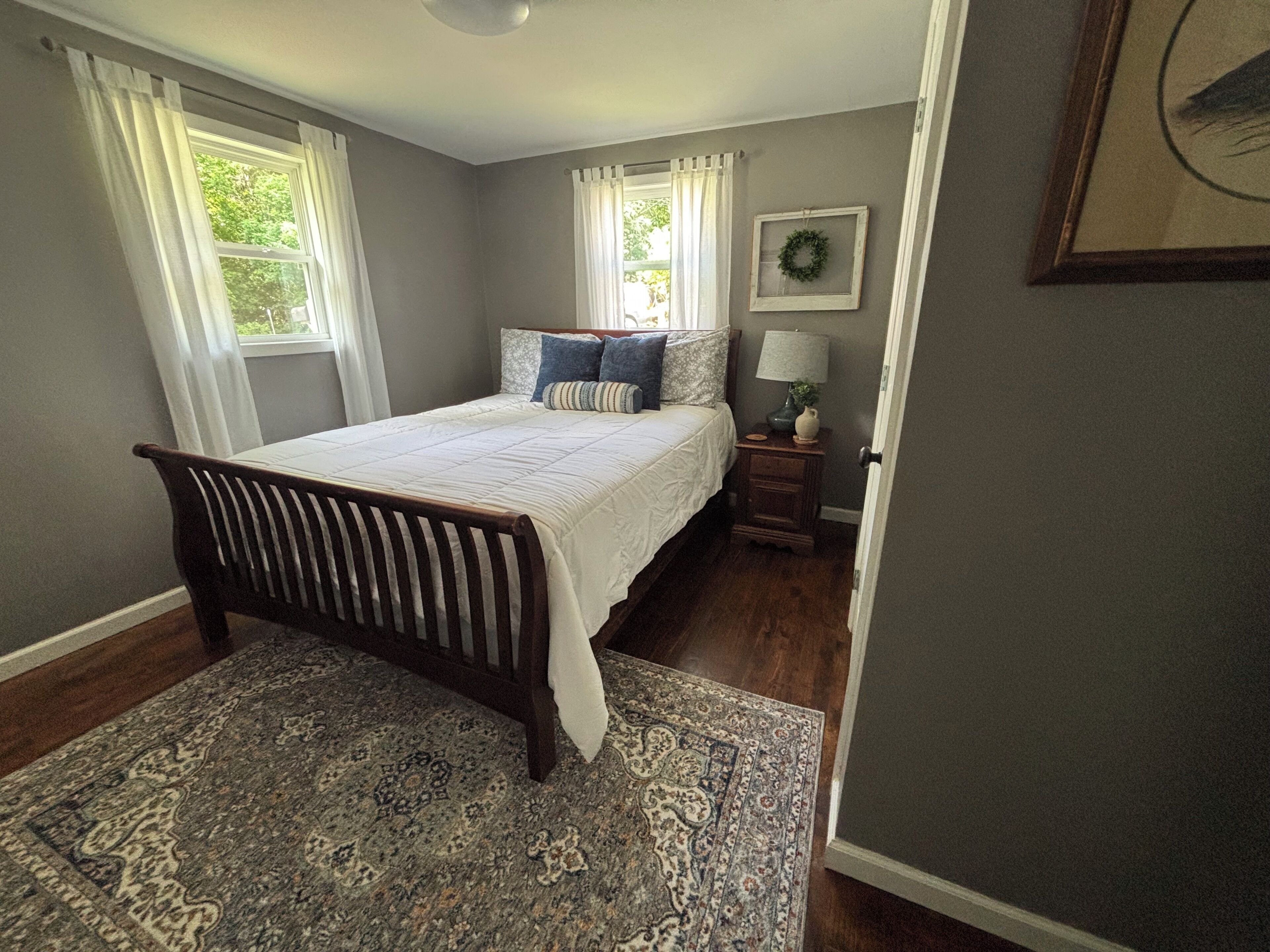 A bedroom with a bed, a nightstand, a lamp, a rug, and a window with curtains.