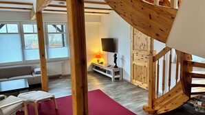 A spacious living area with a wooden staircase, a red rug, a sofa, and a television. - Blue House - arrive and feel at home (Hülseburg)