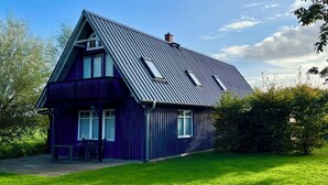 A two-story house with a steep gabled roof, a chimney, and a small porch with a bench. - Blue House - arrive and feel at home (Hülseburg)
