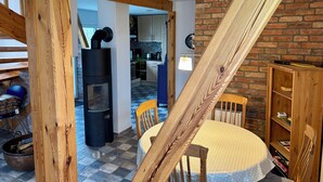 A cozy room with a wooden ceiling, a black wood stove, a round table with chairs, and a brick wall. - Blue House - arrive and feel at home (Hülseburg)