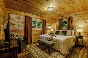 Un dormitorio de cabaña de madera con cama, banco, mesita de noche y una obra de arte en la pared.