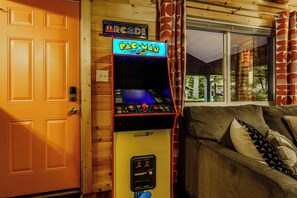 Une borne d’arcade Pac-Man, une porte en bois et un canapé avec des coussins.