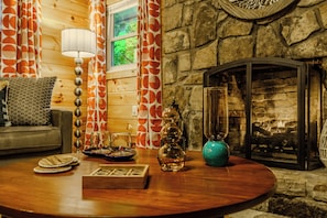 Una sala de estar acogedora con chimenea, una mesa de centro redonda de madera y una cortina estampada.