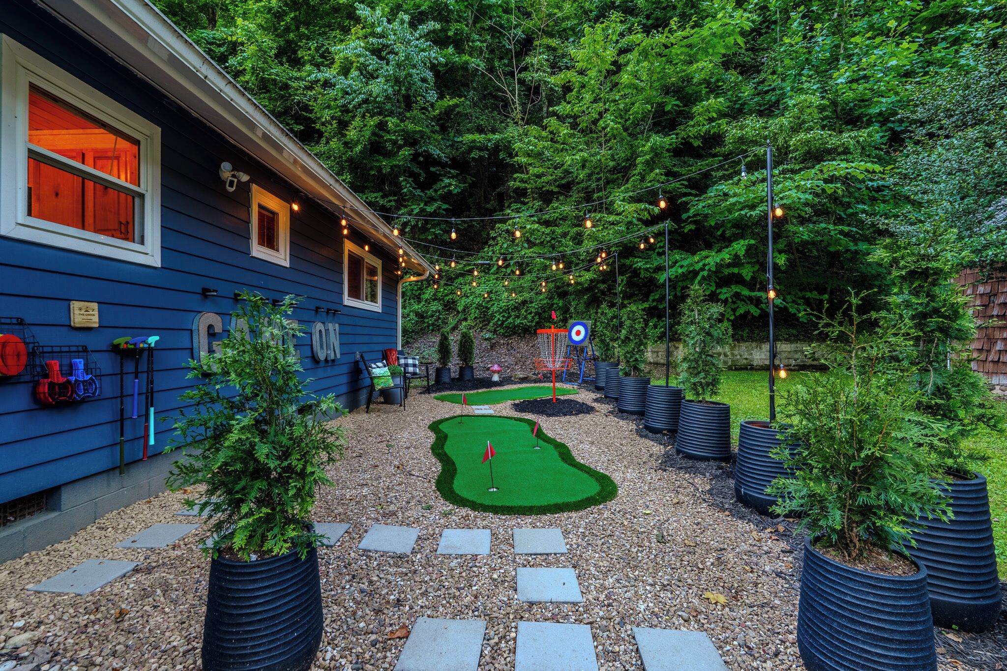 Edifici blau amb un petit jardí que inclou un camp de mini-golf, plantes en testos i una guirlande de llums.
