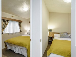 A hotel room with two beds, a window with curtains, a bedside table with a lamp, and a nightstand.