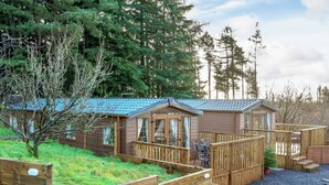 A cabin with a deck, surrounded by a wooden fence and trees.