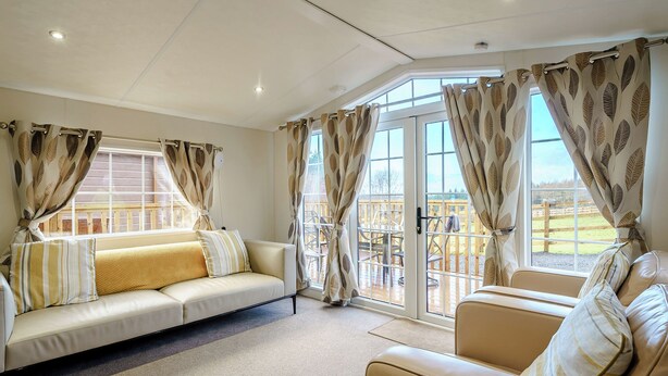 A spacious living room with a beige sofa, a smaller armchair, and a large window with curtains.