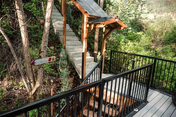 A wooden staircase with a metal railing leading to a deck, surrounded by trees. - Lakefront Hideaway w/ beautiful views, quiet area, private lake access & dock! (Christina Lake)