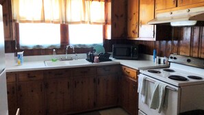 A kitchen with wooden cabinets, a white stove, a microwave, and a sink with a window above it. - Brick House Retreat at the Heart of Hamlet (HAMLET)