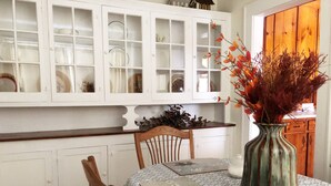 A dining area with a table set for two, a vase with dried plants, and a white cabinet with glass doors above. - Brick House Retreat at the Heart of Hamlet (HAMLET)