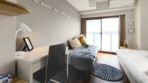 Quarto de hotel moderno com escrivaninha, cadeira, cama e vista da cidade através de grandes janelas.