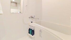Casa de banho com uma banheira branca, um espelho e uma prateleira com artigos de higiene pessoal.