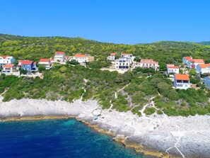A coastal residential area with houses on a hillside, a rocky shoreline, and clear blue water. - Sea View Villa in Cara (Korcula)