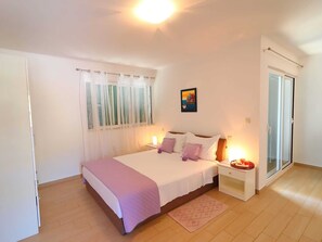 Une chambre à coucher avec un lit, une table de chevet avec une lampe, une fenêtre avec des rideaux et une porte.