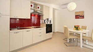 A modern kitchen with a red backsplash, a dining area with a white table and chairs, and a ceiling light fixture. - Modern Apartment in Kastel Stari (Kastela)