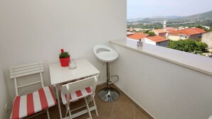 A small balcony with a white table, a red and white striped bench, a potted plant, and a white chair. - Modern Apartment in Kastel Stari (Kastela)