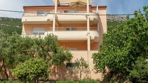A multi-story building with balconies, surrounded by greenery and a mountainous backdrop. - Modern Apartment in Kastel Stari (Kastela)