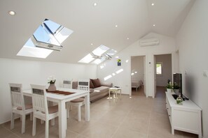 A modern living space with a dining area, sofa, TV, and skylights.