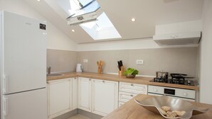 A kitchen with a skylight, white cabinets, a wooden countertop, and a stove.