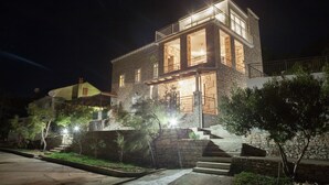 A two-story stone building with a balcony, a staircase, and a well-lit entrance.