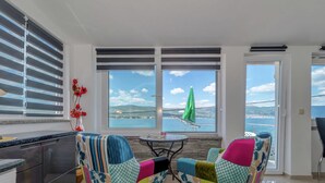 A modern kitchen with a large window, two colorful chairs, a small table, and a view of the sea. - Apartment in Arbanija With Terrace (Trogir)