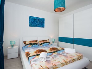 A modern bedroom with a bed, two bedside tables, a wall art piece, and a hanging light fixture.