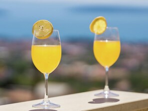 Deux verres d’une boisson jaune, garnis de rondelles de citron, sur un balcon offrant une vue sur la ville.