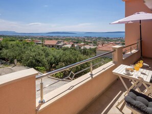 A balcony with a view of a town and sea, a table with drinks, and a cushioned chair. - Sea-view Retreat, Kastel (Kastela)