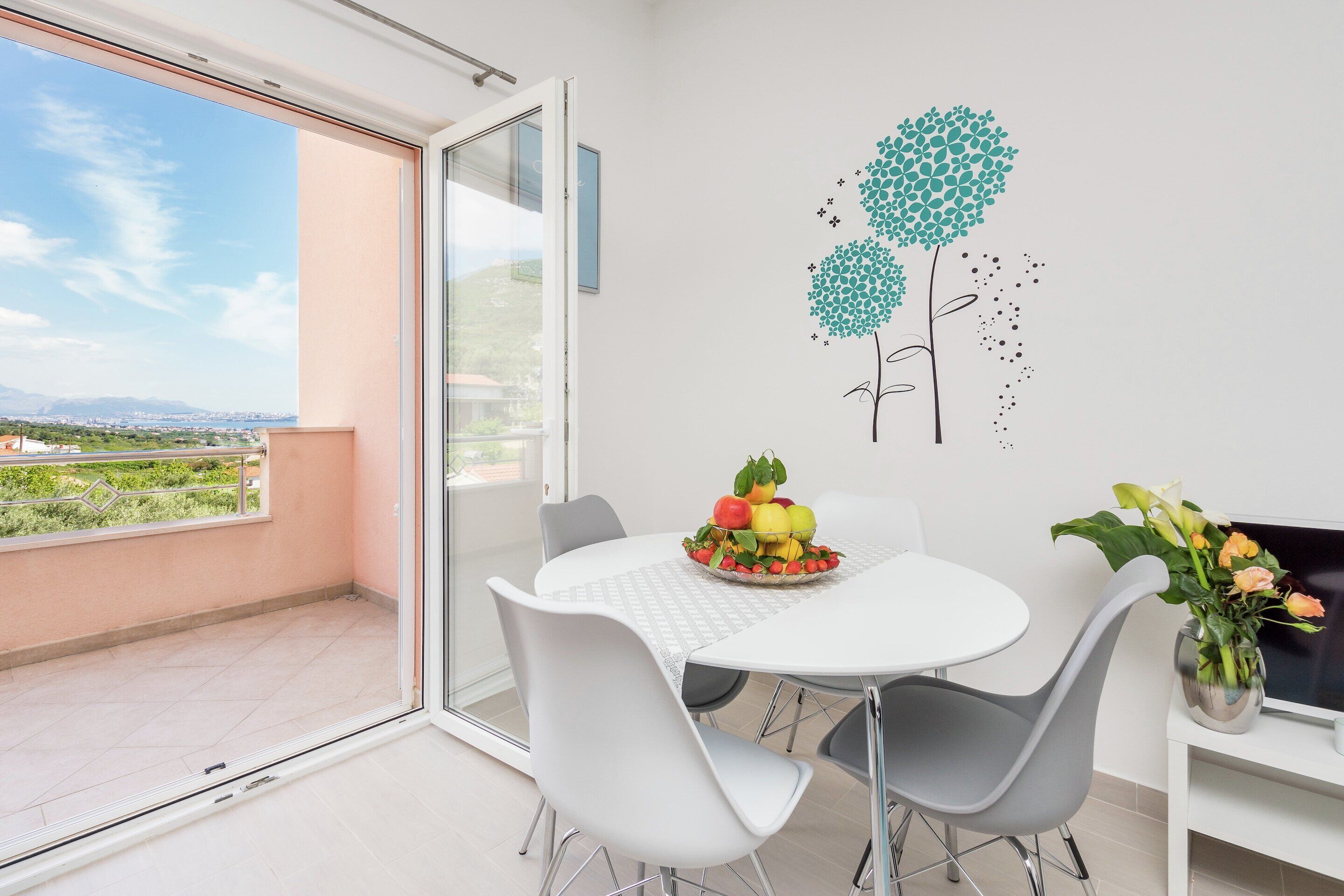 A modern dining area with a white table and chairs, a fruit bowl, and a vase with flowers.