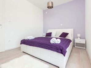 Une chambre moderne avec un lit blanc, une literie violette et un tapis blanc moelleux.