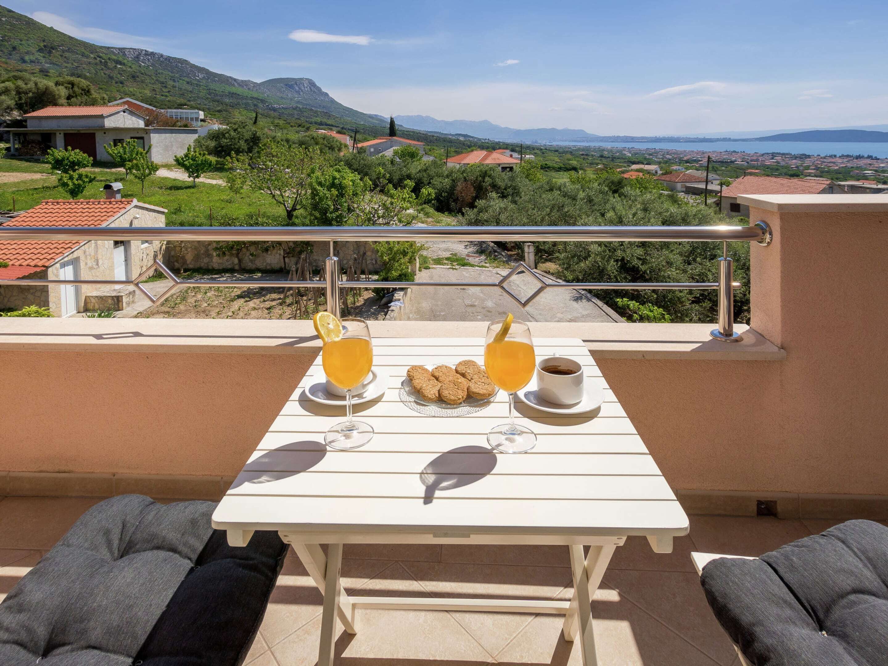 A balcony with a table set for breakfast, overlooking a scenic landscape with houses and mountains.