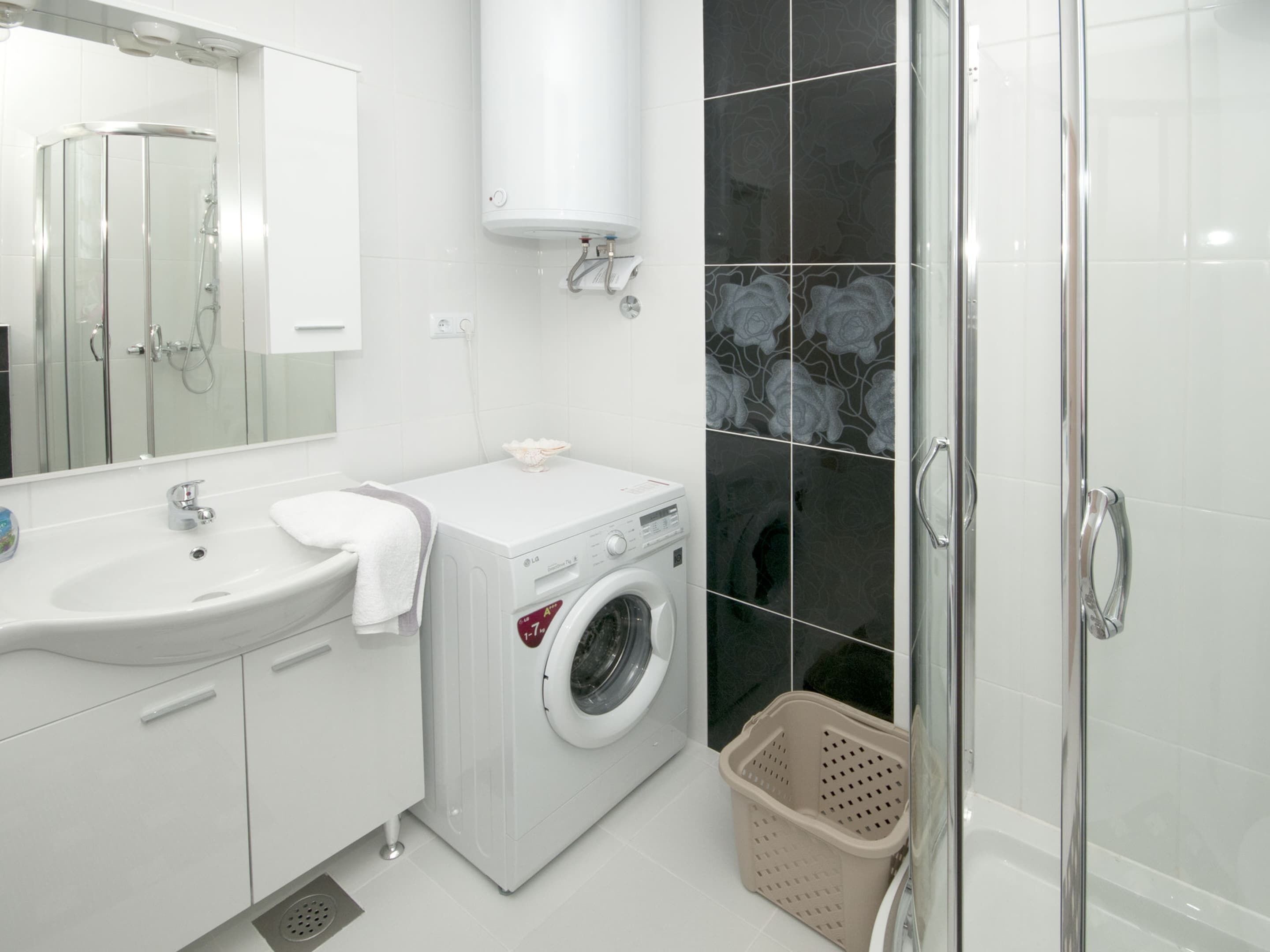 Ein modernes Badezimmer mit Waschbecken, Spiegel, Waschmaschine und Duschkabine aus Glas.