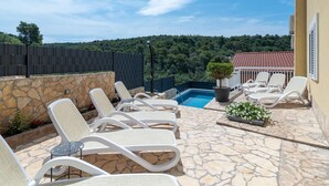 Un espace aménagé au bord de la piscine, avec des chaises longues, une petite piscine et une vue sur une colline boisée.