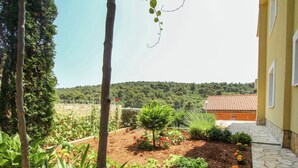 Un jardin où l’on trouve différentes espèces de plantes, ainsi qu’un chemin de pierres qui mène à un bâtiment doté d’un toit en tuiles.