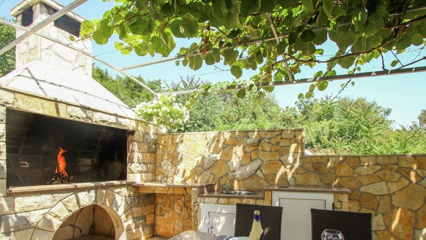 Une cuisine extérieure avec un mur en pierre, un barbecue et un coin repas avec une table dressée pour deux personnes.
