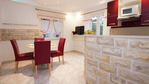 A compact kitchen with a stone accent wall, a dining area with red chairs, and a microwave on the counter. - Apartment 5 km From Trogir's Center (Split)