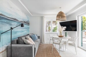 A modern living room with a gray sofa, a black floor lamp, a large painting of a seascape, a woven pendant light, and a dining area with white chairs and a table. - Apartment 5 km From Trogir's Center (Split)