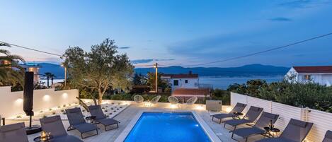 A pool area with lounge chairs and a view of the sea.