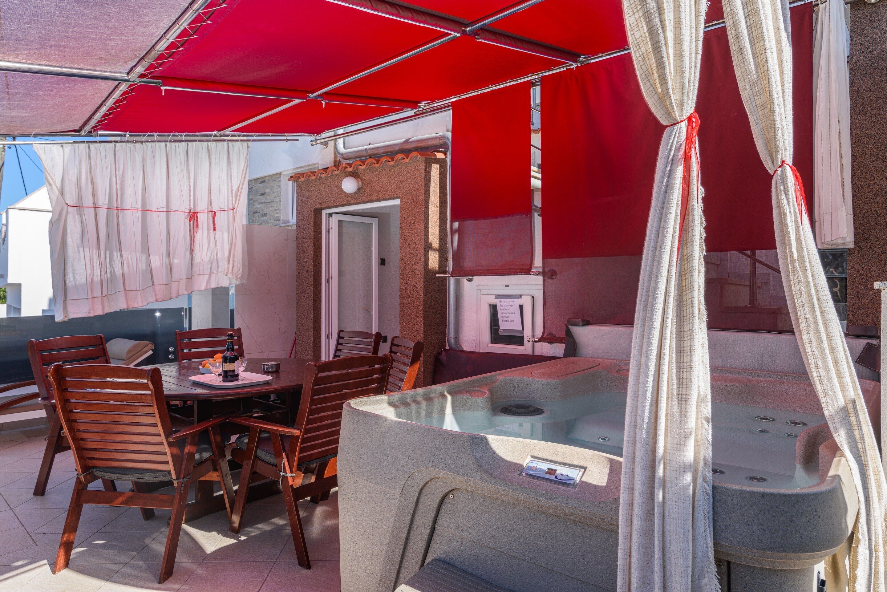 An outdoor patio with a table and chairs, a hot tub, and a covered area with red canopies.