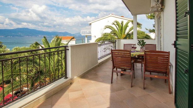 Un balcón con mesa y sillas, con vistas a la costa y montañas al fondo.