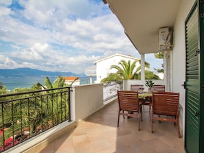 A balcony with a table and chairs, overlooking a coastal view with mountains in the distance. - Modern Apartment With Pool and Terrace (Split)