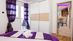 Habitación de hotel con cama, cortinas moradas, piso de madera y vista a la cocina y el comedor.