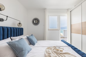 Un dormitorio con cama, almohadas, una lámpara de noche, decoración en la pared y vistas al exterior.