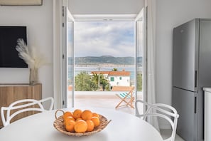 Una cocina moderna con vistas a un pueblo costero, una mesa de comedor con una cesta de naranjas y una silla blanca.
